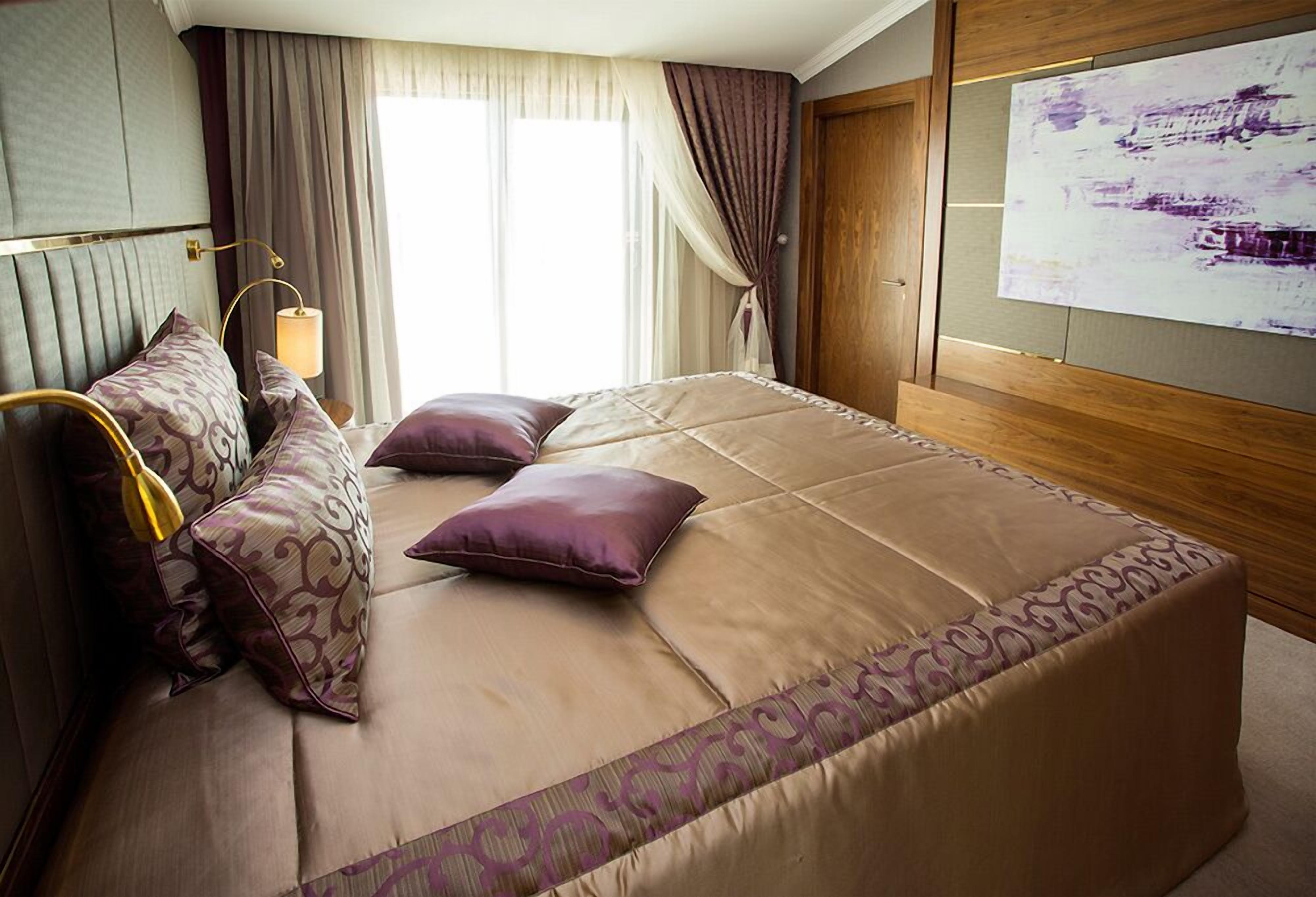 A hotel room with a large bed, a bedside lamp, and a view of the outdoors through the window.