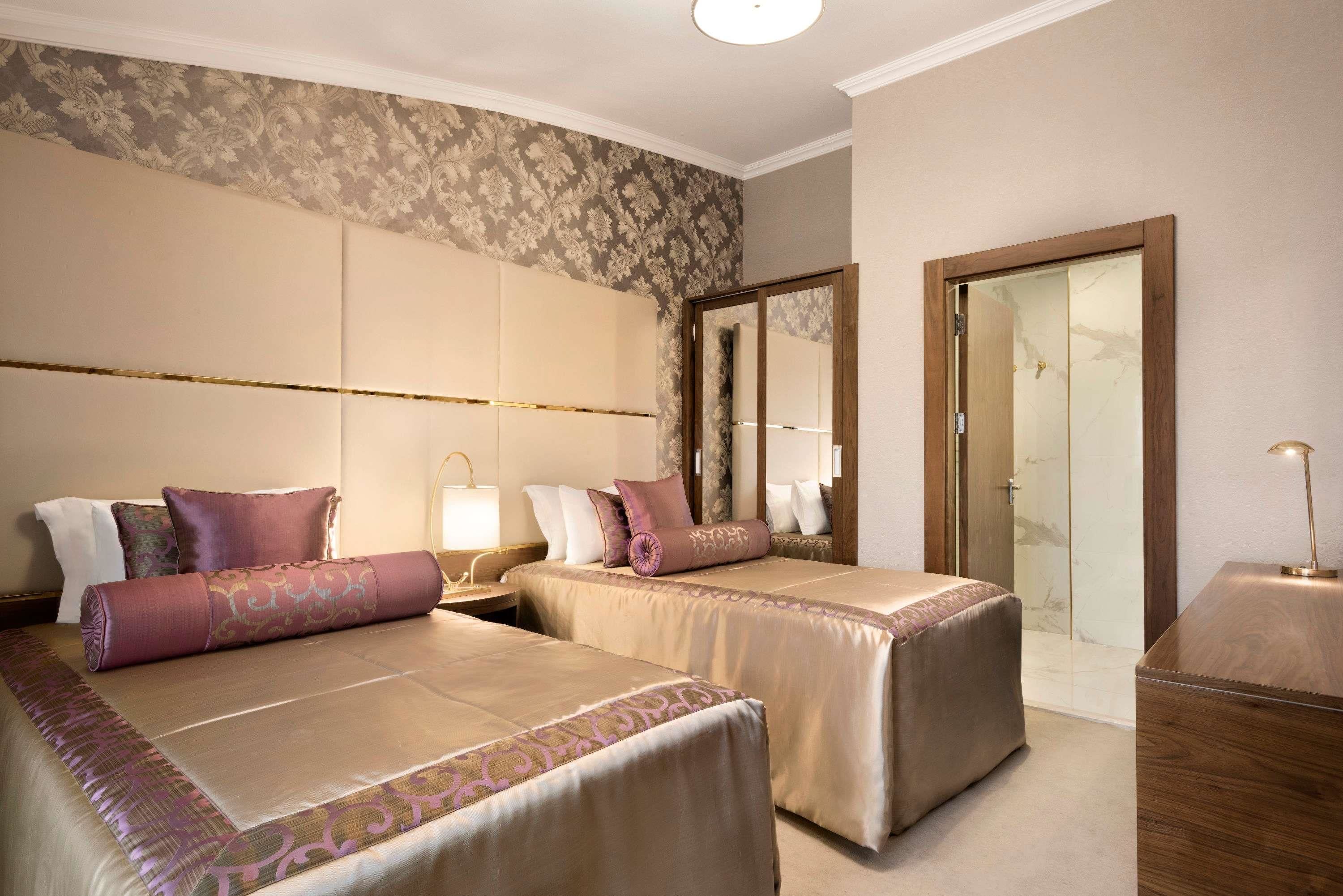Una camera d'albergo con due letti, un grande specchio e un comodino in legno.