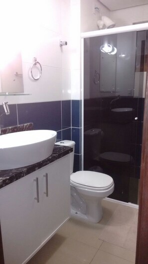 Un baño con un lavamanos blanco, inodoro y cabina de ducha con mampara de vidrio.