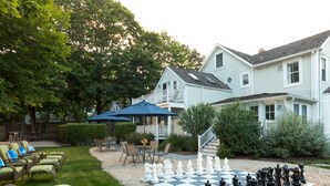 A backyard with a large chessboard, outdoor furniture, and a house. - West Neck Guesthouse (Shelter Island Heights)