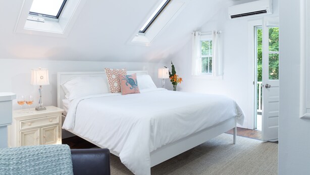 A bedroom with a bed, bedside tables, a lamp, a window, and a door. - West Neck Guesthouse (Shelter Island Heights)