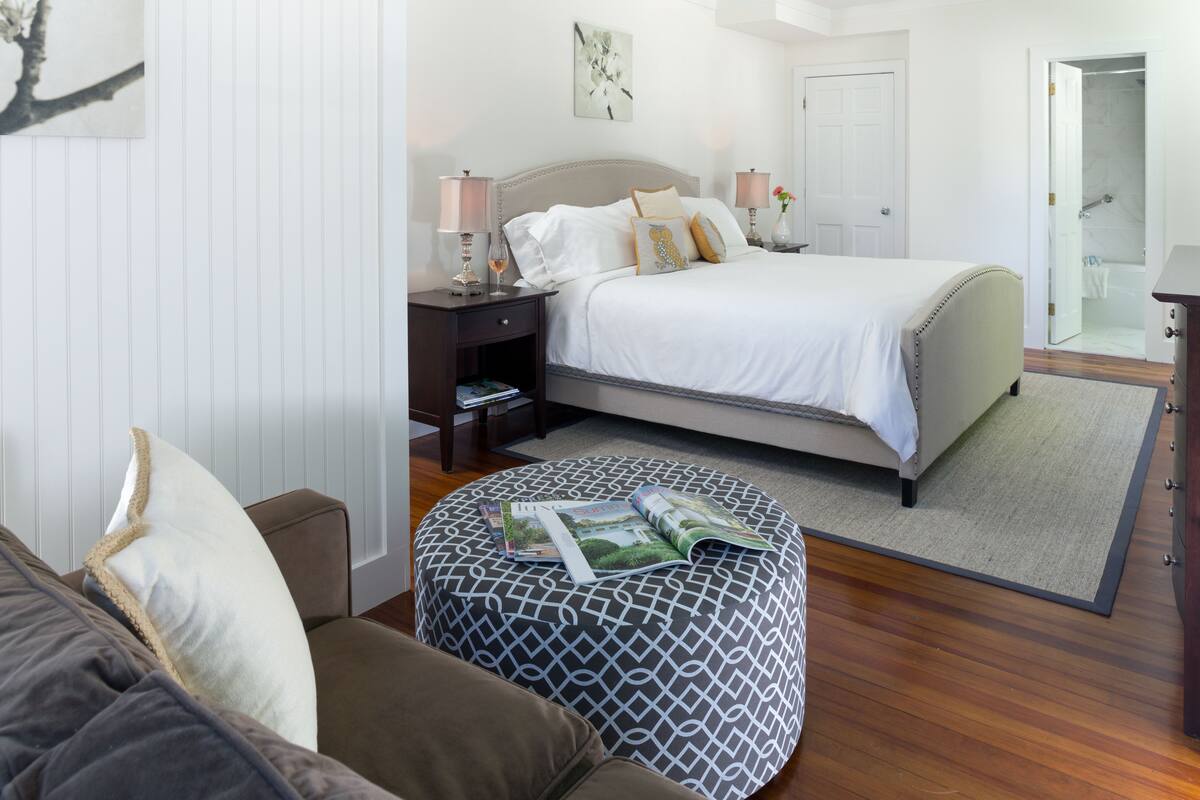 A bedroom with a bed, nightstands, a bedside table, a lamp, a magazine, and a window.