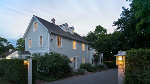 A large, light blue two-story house with a steep roof, surrounded by greenery and a gravel driveway. - West Neck Guesthouse (Shelter Island Heights)