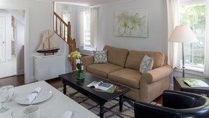 A living room with a beige sofa, a coffee table, and a dining table set with plates and glasses. - West Neck Guesthouse (Shelter Island Heights)