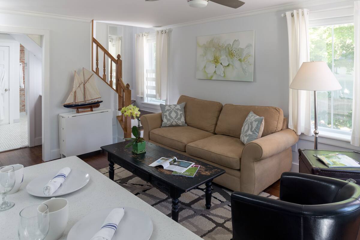 A living room with a beige sofa, a coffee table, and a dining table set with plates and glasses.