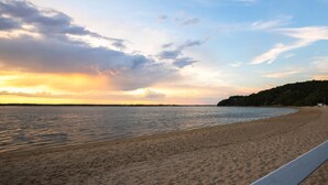 A beach with a wooden walkway along the shore, calm water, and a sunset sky. - West Neck Guesthouse (Shelter Island Heights)