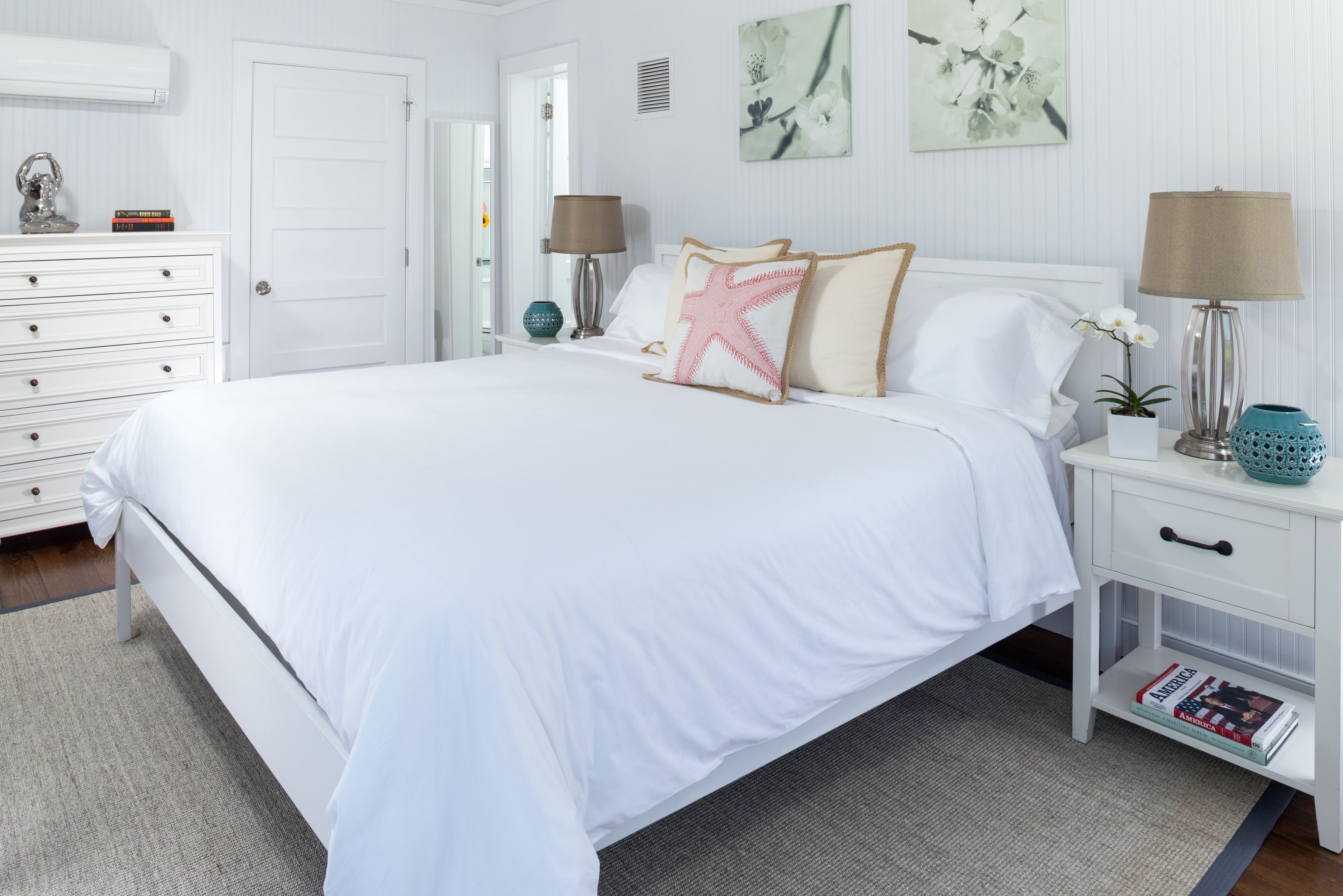 A white bedroom with a large bed, two bedside tables, a dresser, and a door.