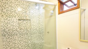 A bathroom with a glass shower enclosure, a toilet, a sink, and a window above the sink. - Pousada NOVA ESTRELA INN (Búzios)