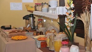 A buffet setup with various food items, including bread, pastries, and a fruit platter. - Pousada NOVA ESTRELA INN (Búzios)