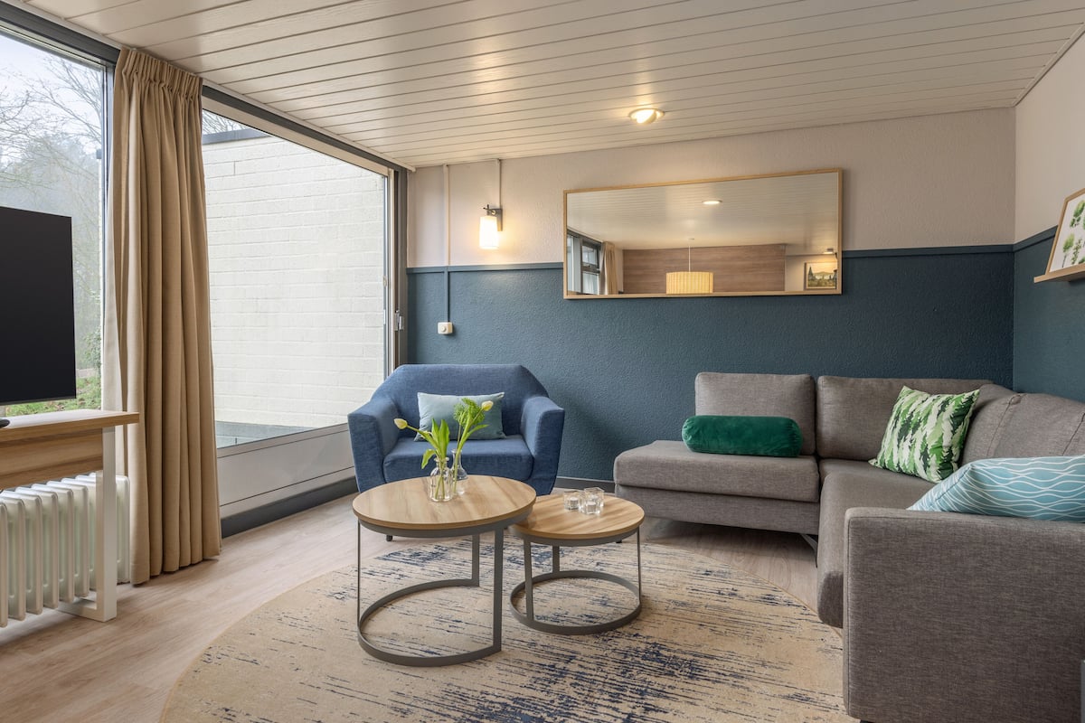 Una sala de estar moderna con un sillón azul, un sofá gris y una mesa de centro redonda.