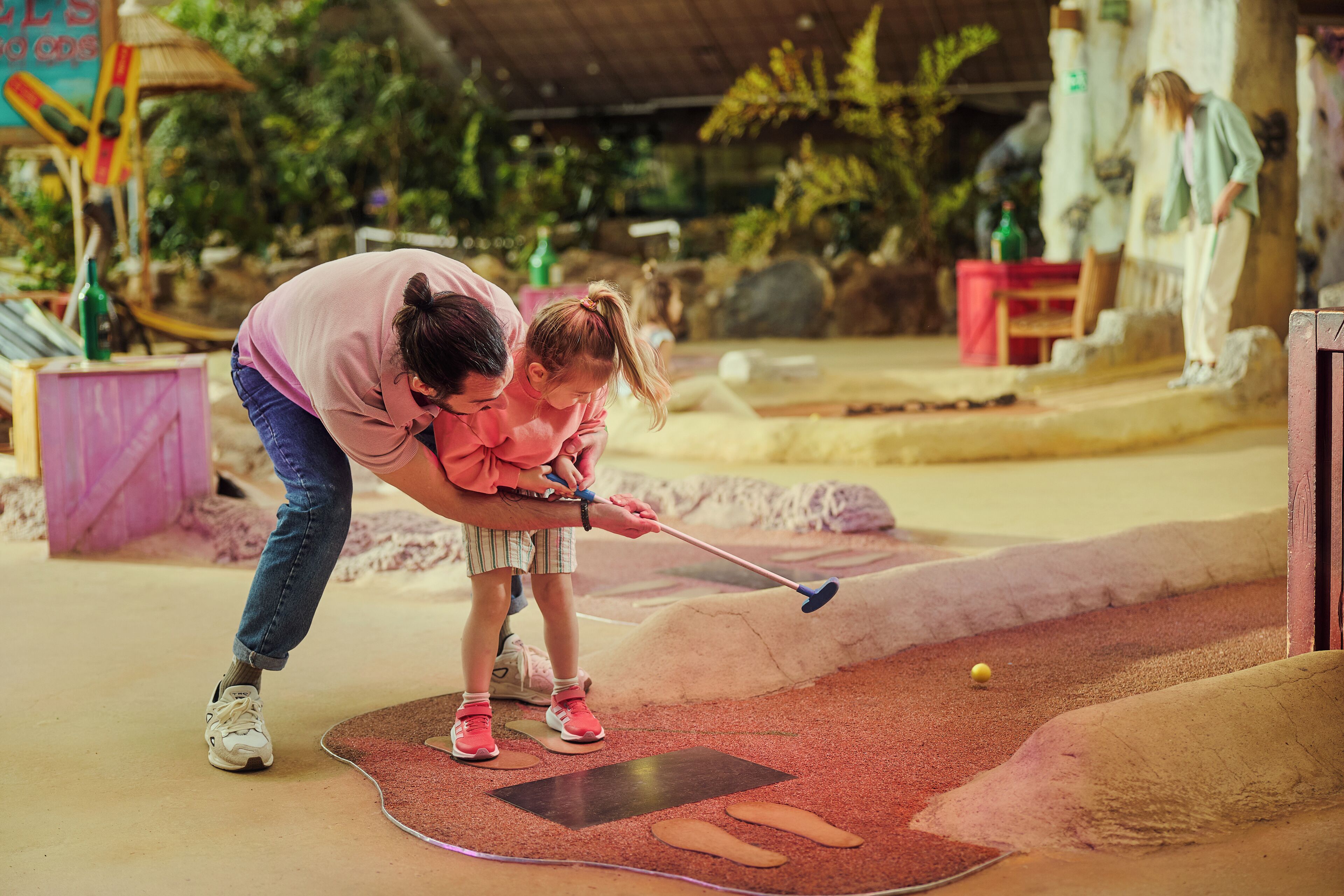 Une personne jouant au mini-golf avec un enfant.