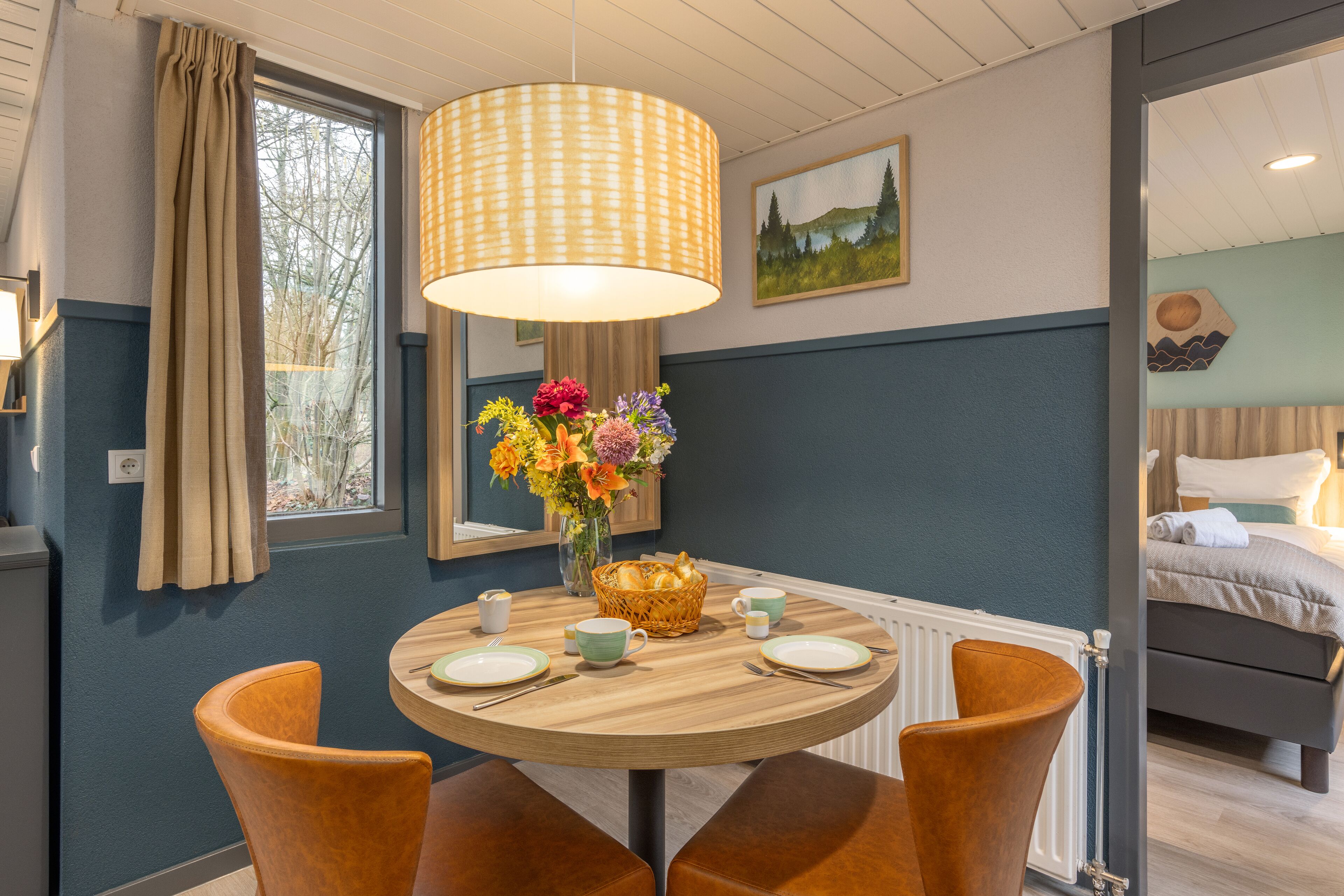 A dining area with a round table, chairs, a vase of flowers, and a hanging light fixture.