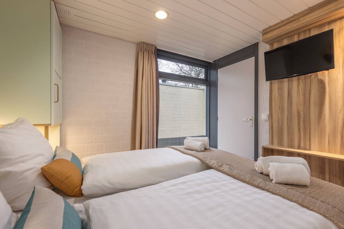 Un dormitorio con dos camas, un televisor montado en la pared y una ventana con cortinas.