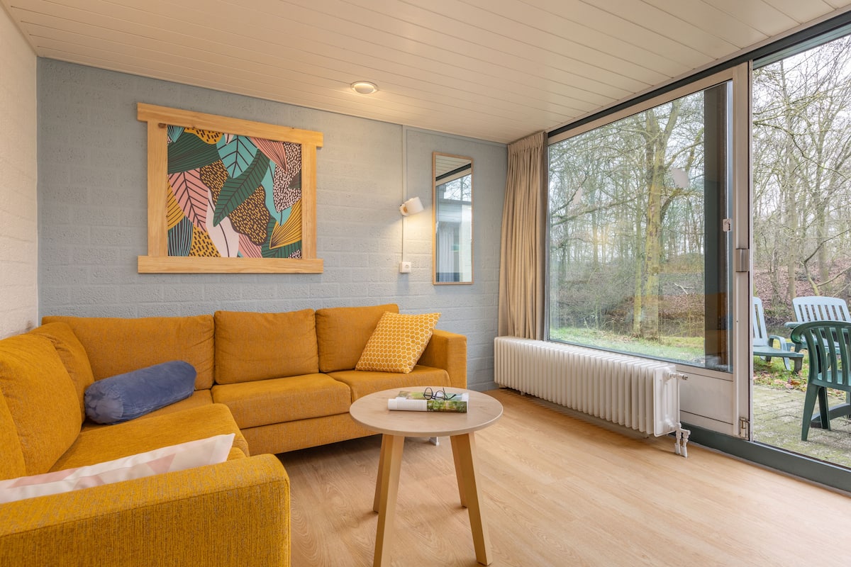 Una sala de estar moderna con un sofá color mostaza, una mesa de centro redonda y un ventanal con vistas al exterior.