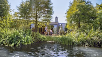 A house with a water feature in front, surrounded by tall grass and trees.