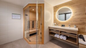 A modern bathroom with a glass-enclosed shower, wooden vanity, and a round mirror with a light. - Center Parcs Het Heijderbos (Heijen)