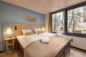 A hotel room with two beds, wooden headboards, and a large window with a view of trees. - Center Parcs Het Heijderbos (Heijen)