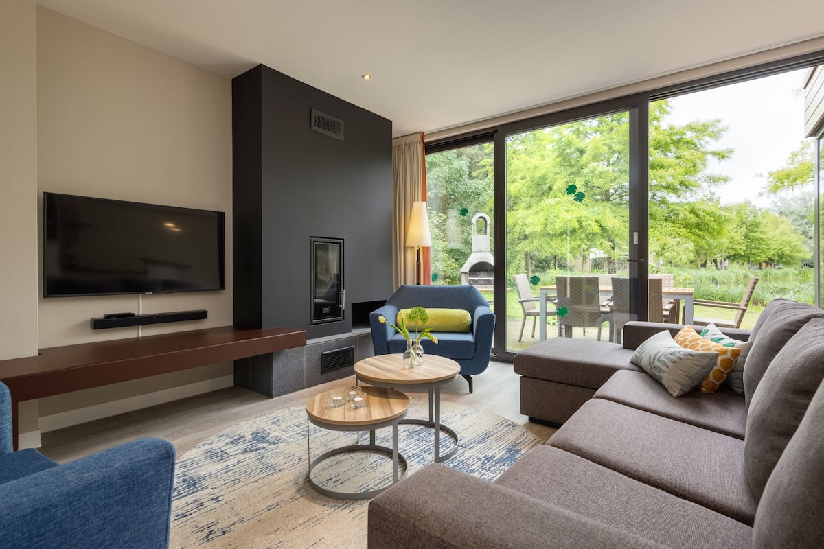 A modern living room with a flat-screen TV, a sofa, a blue armchair, and a dining area with a table and chairs.