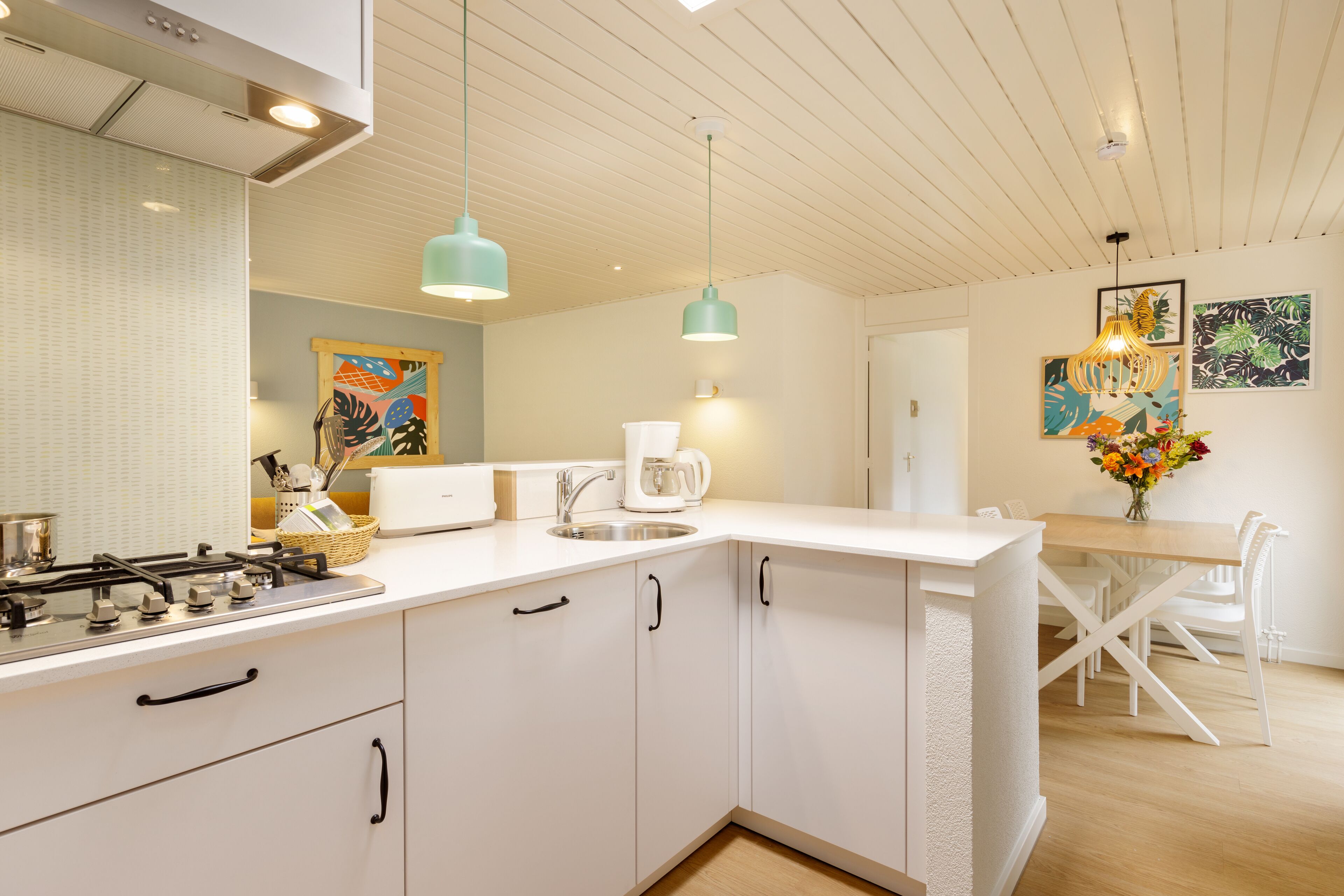 A modern kitchen with white cabinets, a gas stove, and a sink. There is a dining area with a wooden table and chairs.