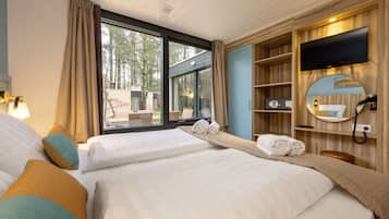A hotel room with two beds, a TV, a mirror, and a window with a view of trees.