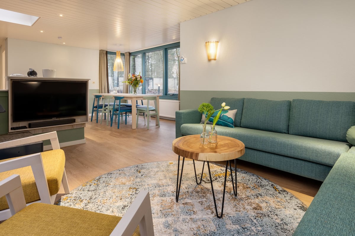 A modern living room with a green sofa, a wooden coffee table, and a flat-screen TV.