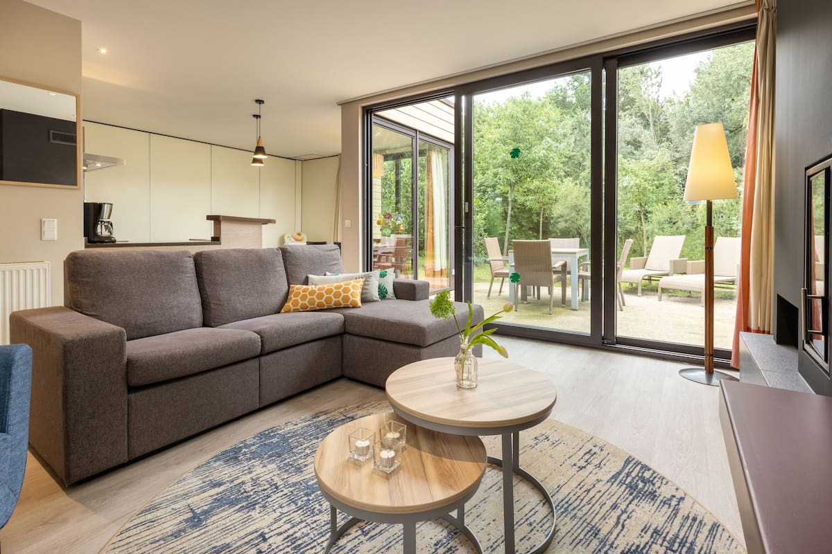 A modern living room with a sectional sofa, a small round table, and a view of the outdoors through large sliding glass doors.