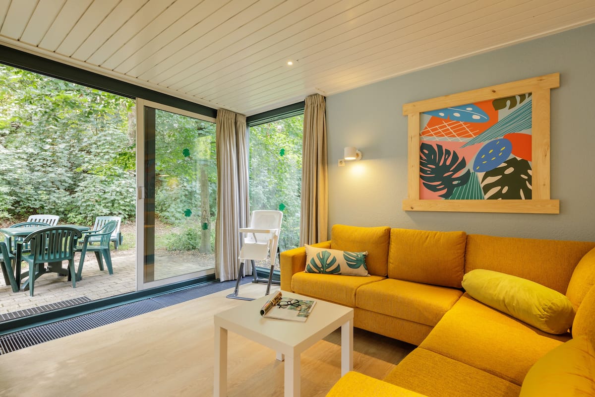 A modern living room with a yellow sofa, a white coffee table, and a large window overlooking a garden.