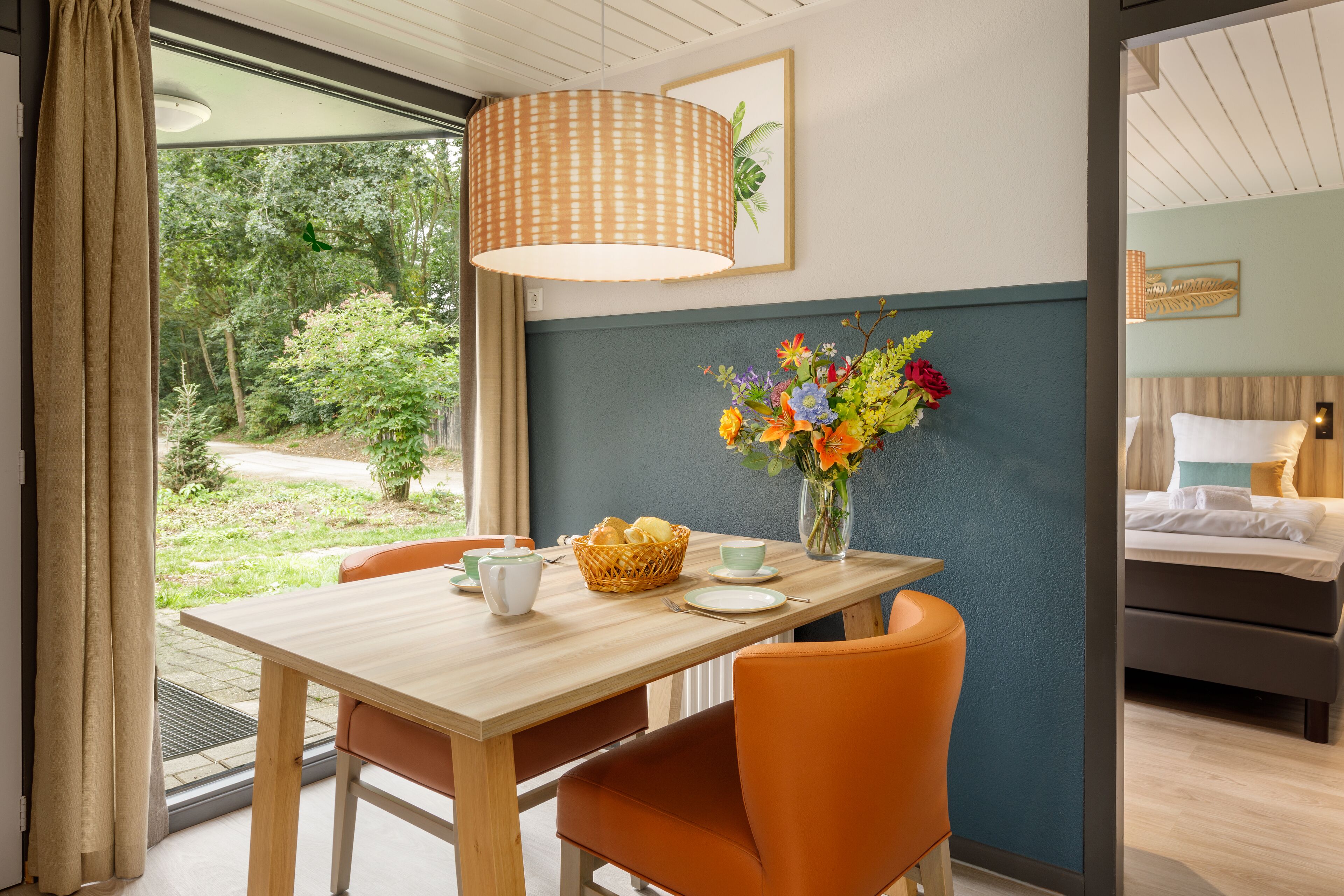 Een eetgedeelte met een houten tafel, oranje stoelen, een vaas met bloemen en een mand met brood.