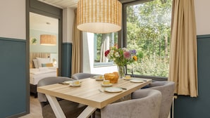 A dining area with a wooden table set for four, a vase with flowers, and a view of greenery outside. - Center Parcs Het Heijderbos (Heijen)