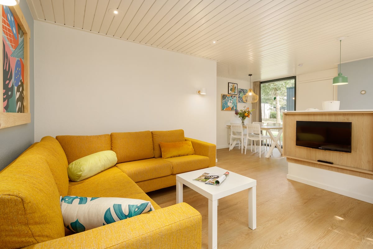 A modern living room with a yellow sofa, a white coffee table, and a flat-screen TV mounted on a wooden cabinet.