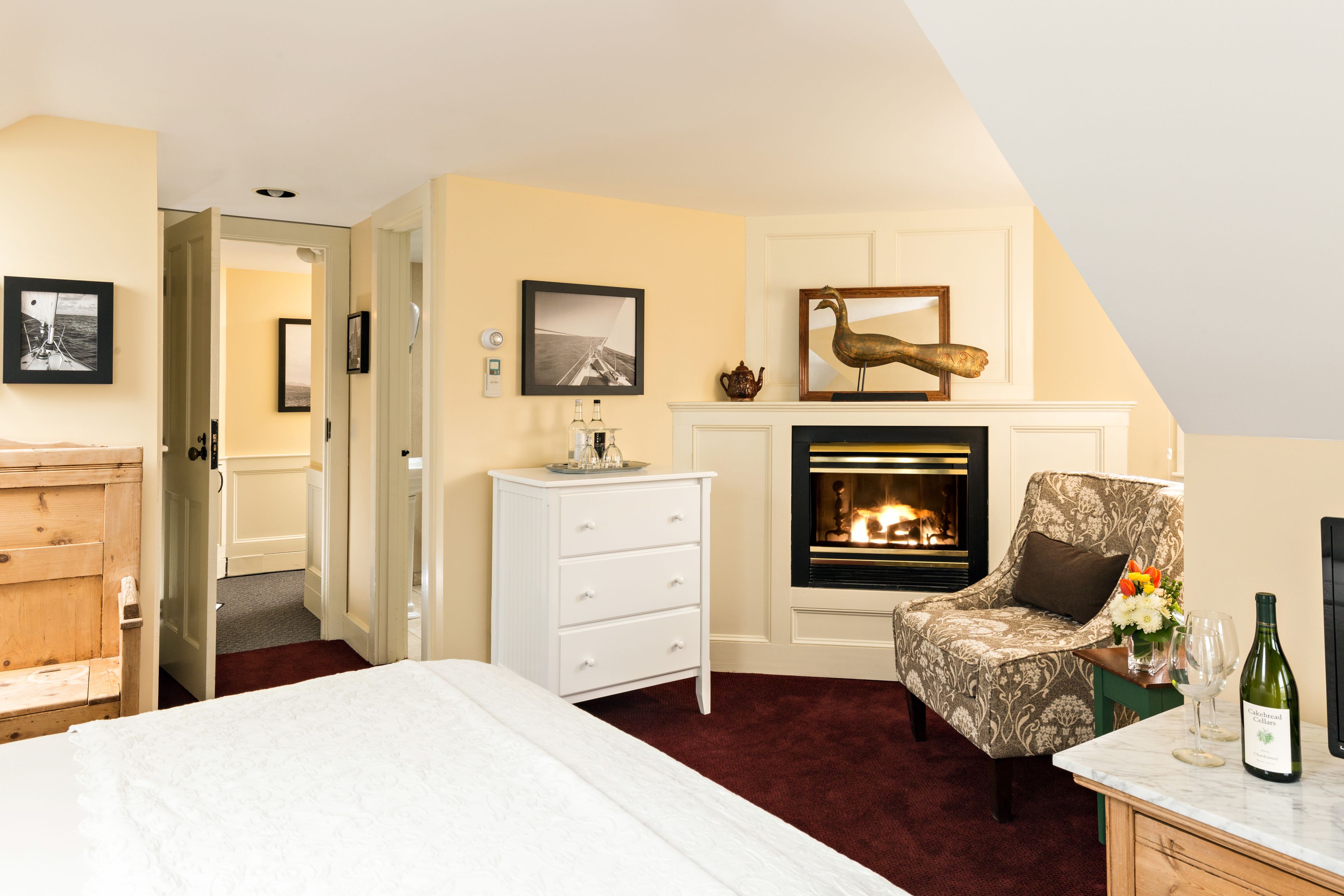A bedroom with a fireplace, a bed, a chair, and a dresser.