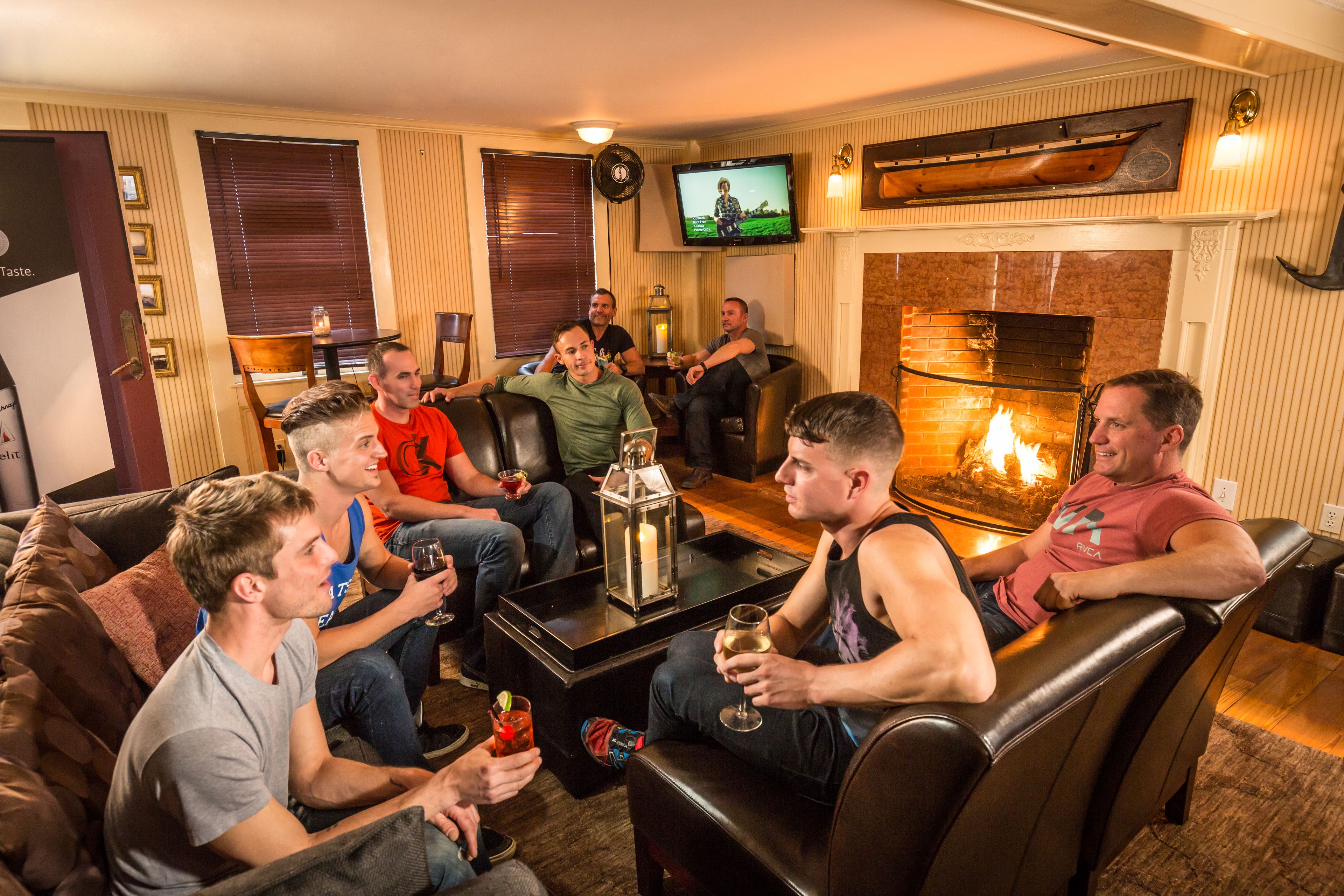 Un grupo de personas en una sala de estar acogedora con chimenea, sofás de cuero y televisión.