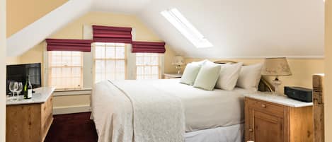 A bedroom with a large bed, wooden nightstands, a desk with a lamp, and a TV.