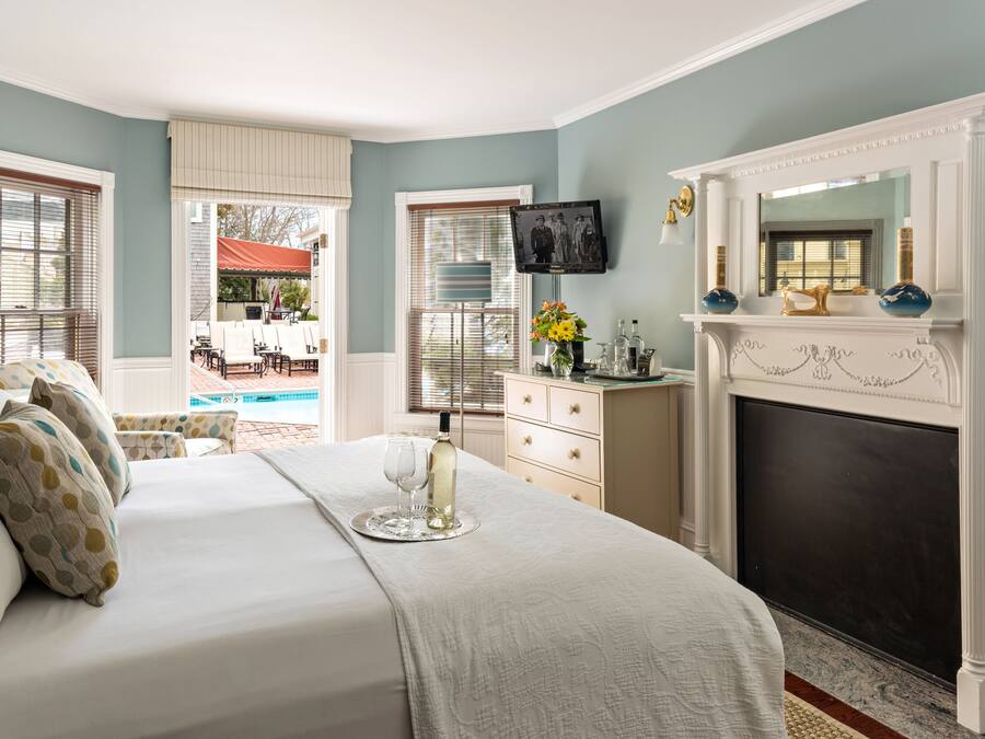 A bedroom with a bed, a fireplace, a television, and a view of the outside.