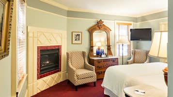 Quarto de hotel com lareira, duas poltronas, cama, cômoda e televisão.
