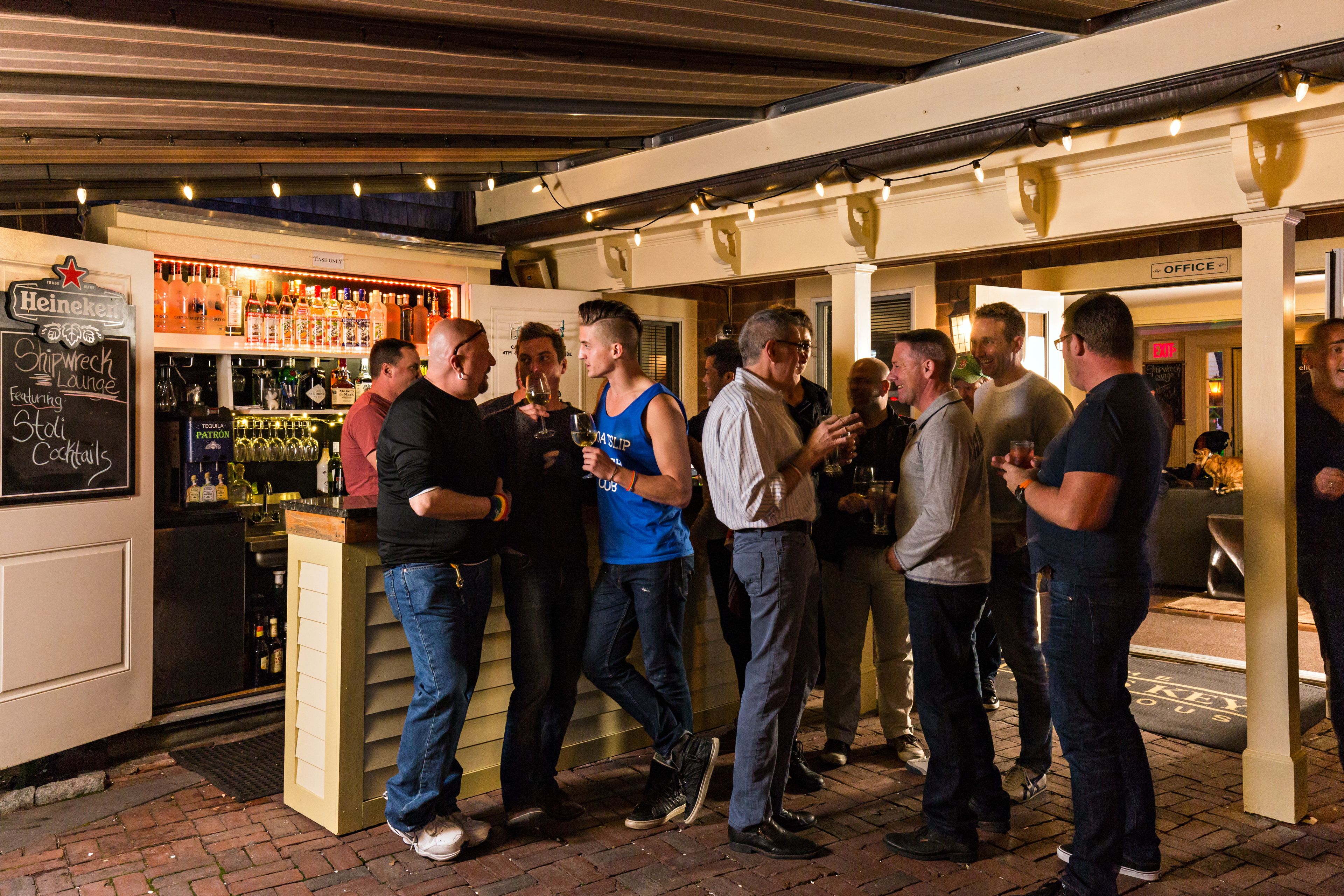 Un groupe de personnes se tient dans un bar, près du comptoir et des étagères remplies de bouteilles.
