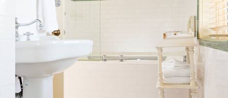 Un baño con lavamanos blanco, ducha con cerramiento de vidrio, bañera y suelo de baldosas.