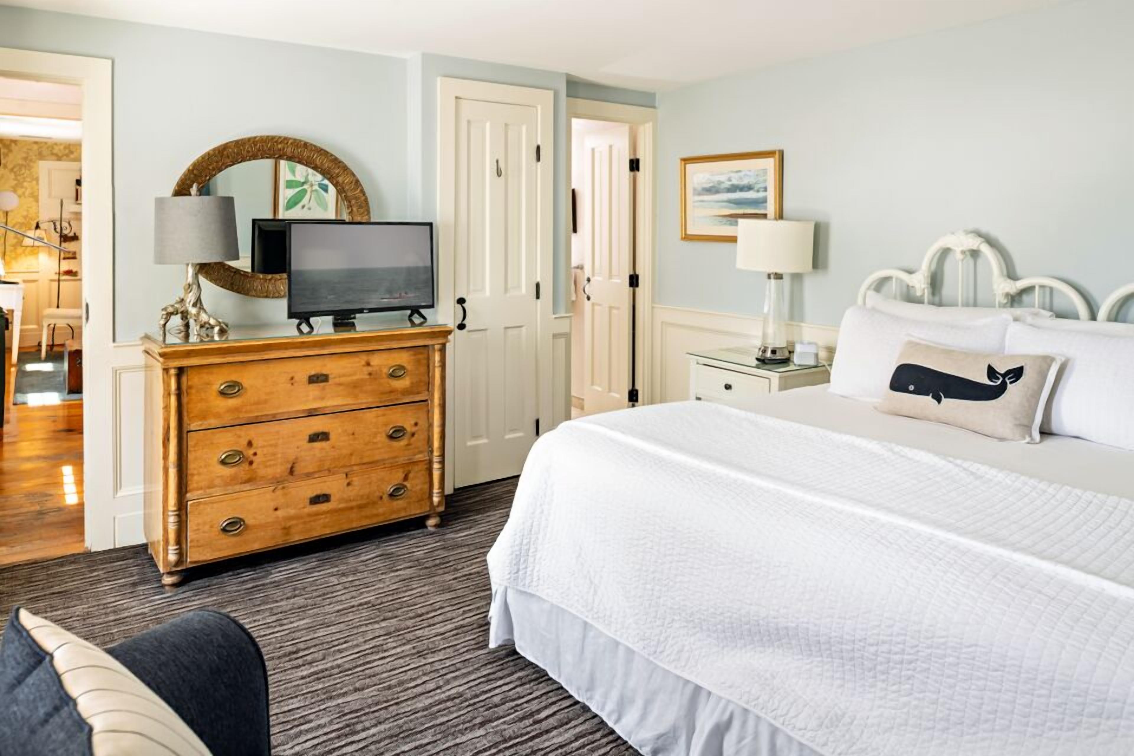 A hotel room with a large bed, a wooden dresser, a television, and a door leading to another room.