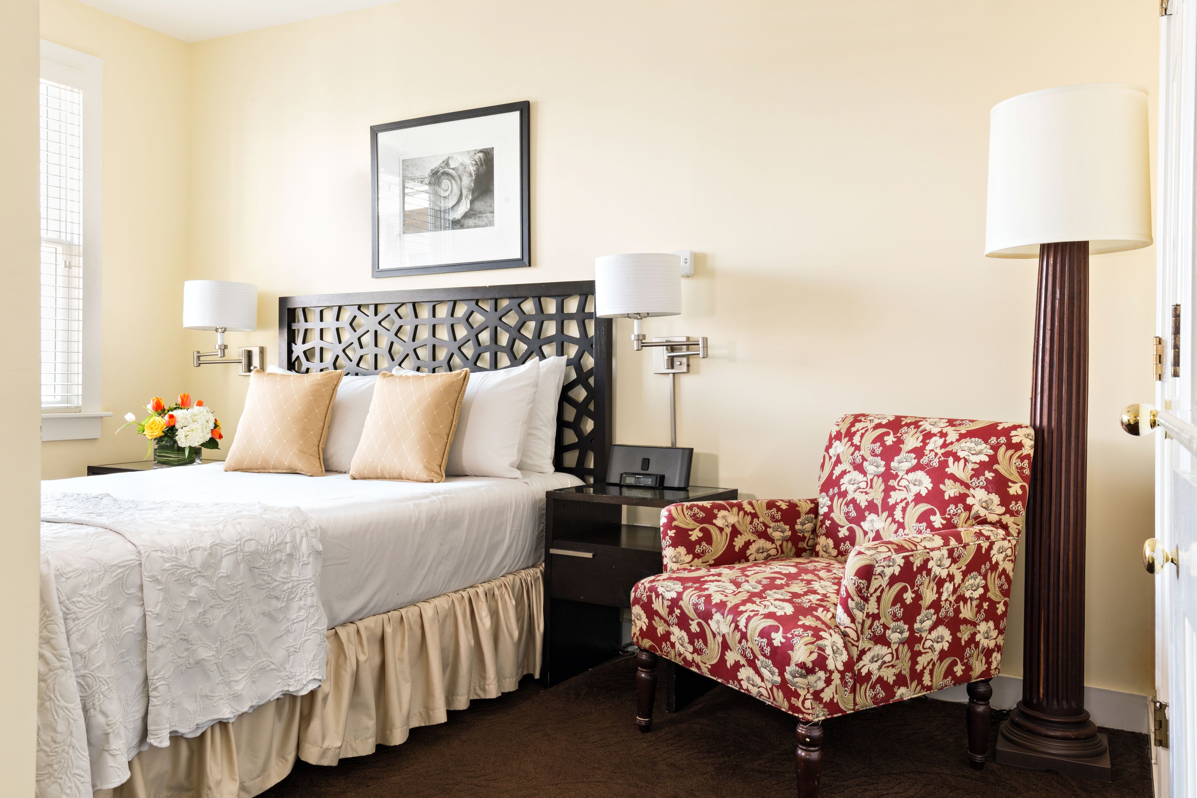 A neatly arranged hotel room with a bed, a desk, a chair, and a lamp.