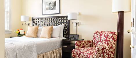 A neatly arranged hotel room with a bed, a desk, a chair, and a lamp.