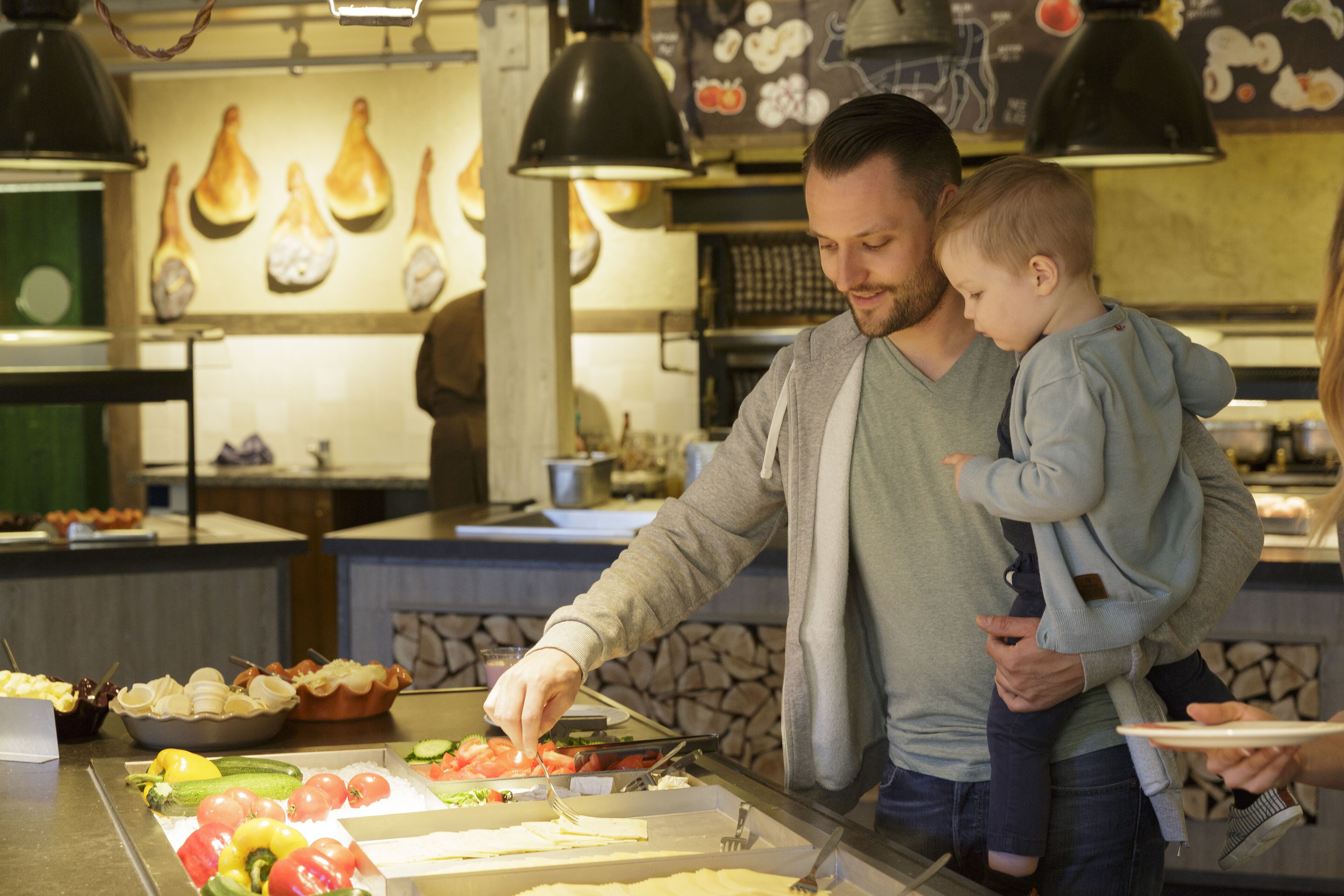 Zona de menjar a buffet amb diversos plats i una persona servint menjar a un nen.