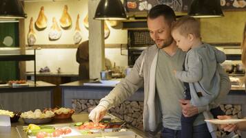 Zona de menjar a buffet amb diversos plats i una persona servint menjar a un nen.