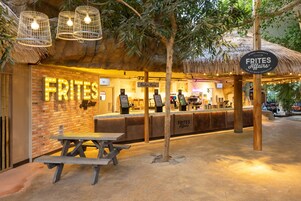 Un restaurante con pared de ladrillo, letrero de neón y zona de mesas al aire libre.