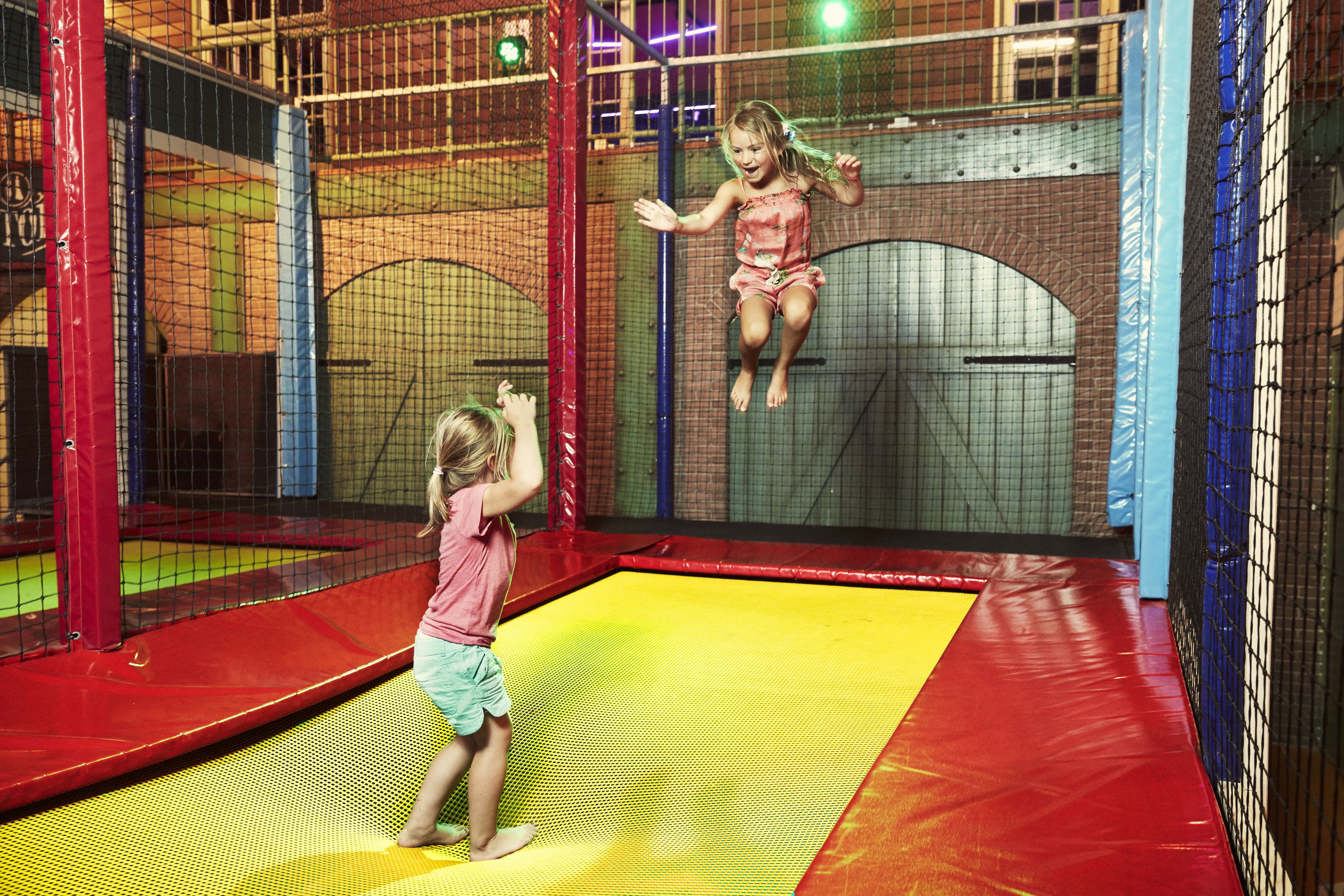 A child jumping on a trampoline inside a play area with safety netting.