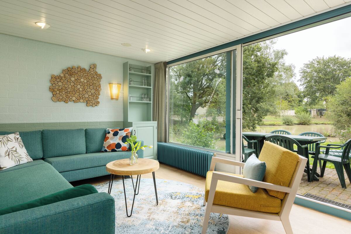 A modern living room with a sofa, a round coffee table, and a chair. There is a large window with a view of greenery outside.