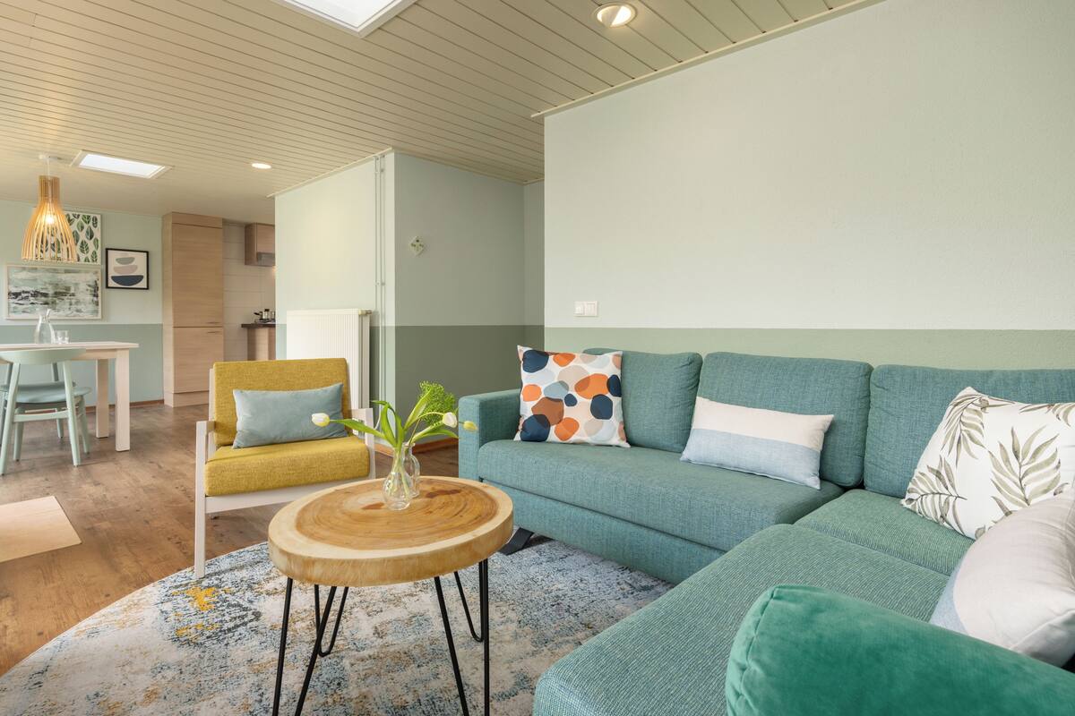 A modern living room with a sofa, a round wooden coffee table, and a dining area with a table and chairs.