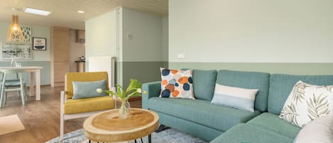 A modern living room with a sofa, a round wooden coffee table, and a dining area with a table and chairs.