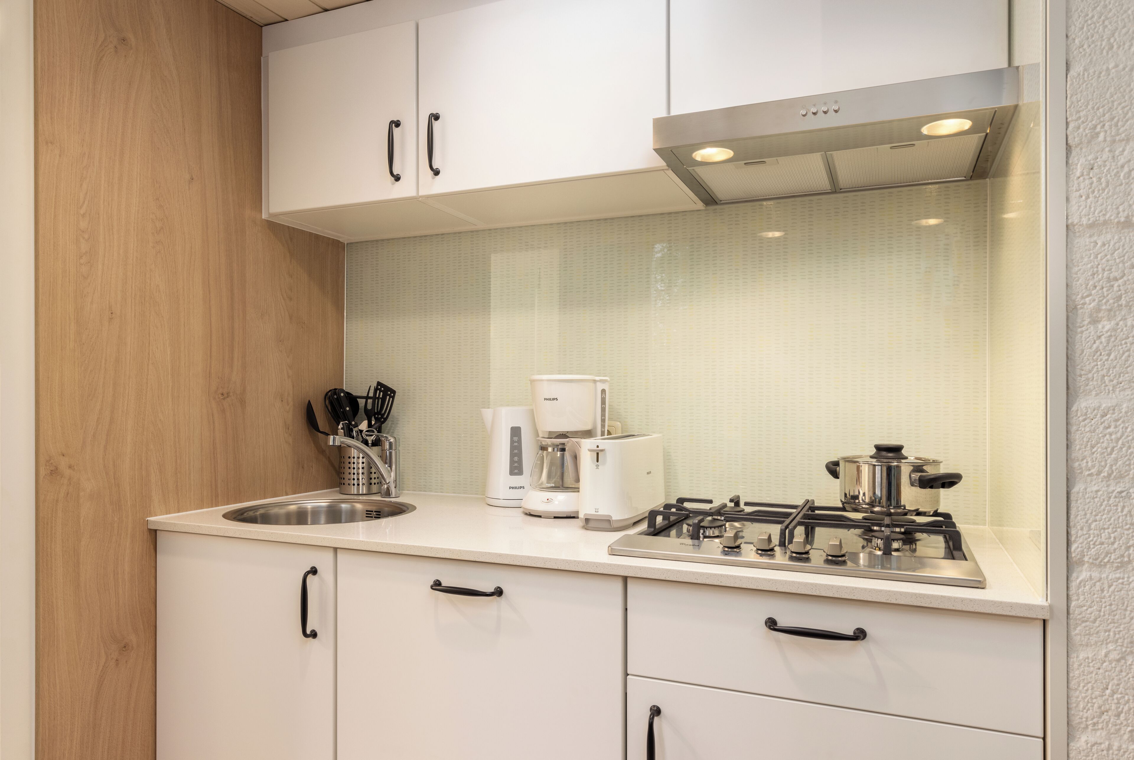 A modern kitchen with white cabinets, a stainless steel sink, a coffee maker, and a gas stove.
