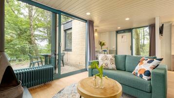Sala de estar moderna com um sofá verde, uma mesa de centro redonda de madeira e uma grande janela com vista para o exterior.