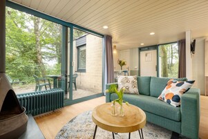 Un salón moderno con un sofá verde, una mesa de centro redonda de madera y un amplio ventanal con vistas al exterior.